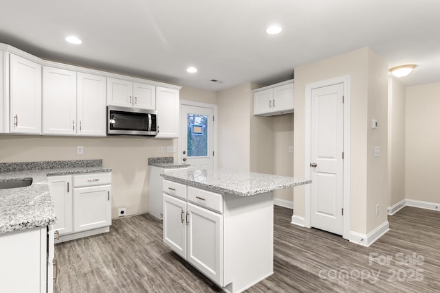 kitchen with white cabinetry, dark hardwood / wood-style flooring, a center island, and light stone counters