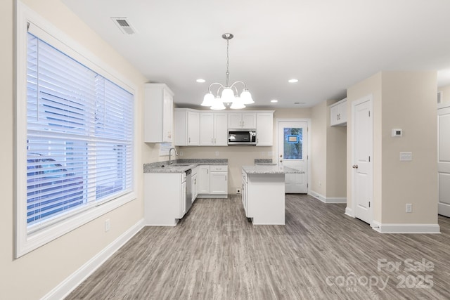 kitchen with a kitchen island, visible vents, white cabinets, hanging light fixtures, and stainless steel microwave