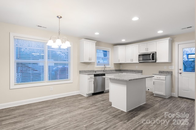 kitchen with stainless steel appliances, white cabinets, a kitchen island, and decorative light fixtures