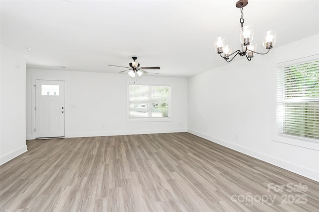 unfurnished living room featuring ceiling fan with notable chandelier, light wood-type flooring, and baseboards