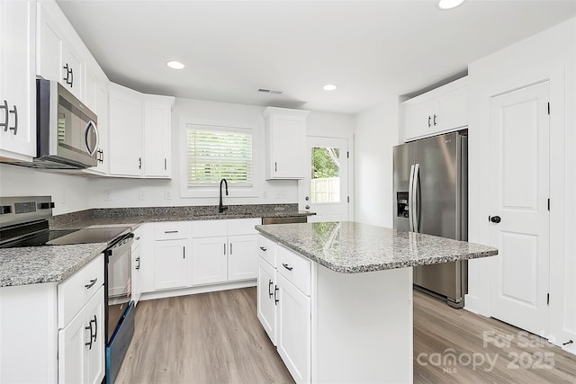 kitchen featuring recessed lighting, light stone counters, light wood finished floors, a sink, and stainless steel appliances