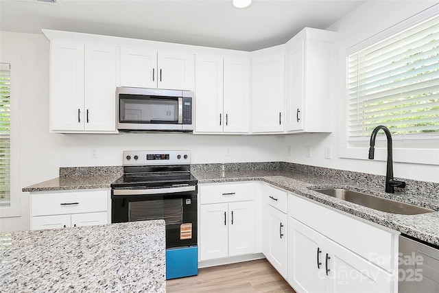 kitchen featuring a sink, stainless steel appliances, light wood-type flooring, and light stone countertops