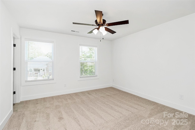 carpeted empty room with baseboards, a ceiling fan, and visible vents