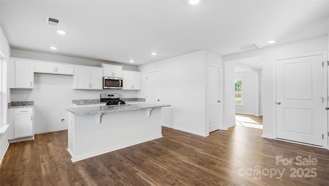 kitchen featuring a kitchen island with sink, light stone counters, stainless steel appliances, and white cabinetry