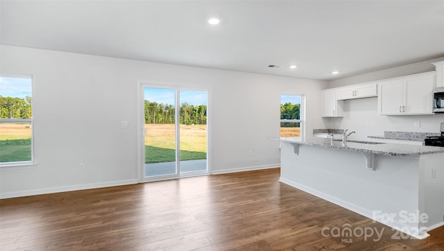 kitchen featuring sink, a breakfast bar, white cabinetry, dark hardwood / wood-style floors, and light stone counters