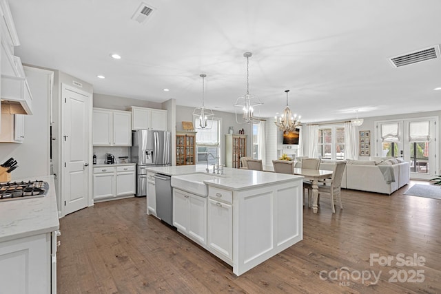 kitchen with stainless steel appliances, decorative light fixtures, an island with sink, and white cabinets