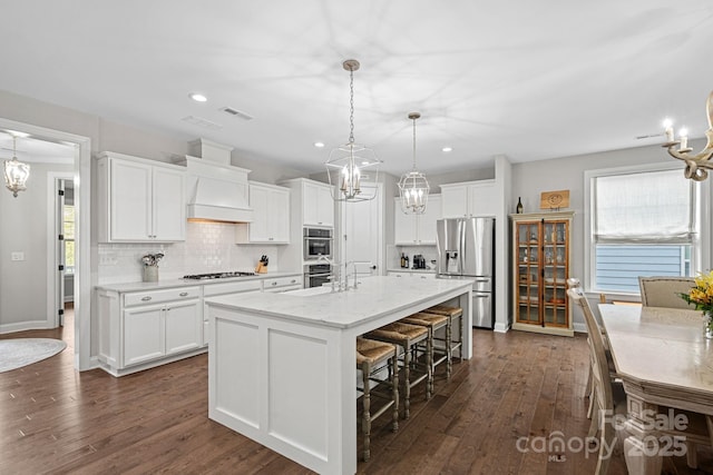 kitchen featuring a center island with sink, white cabinets, pendant lighting, stainless steel appliances, and backsplash