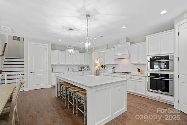 kitchen with a kitchen island with sink, white cabinetry, decorative light fixtures, and custom range hood