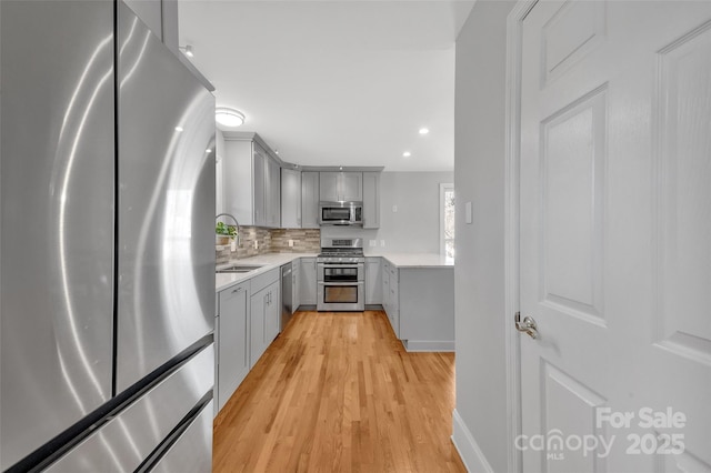 kitchen featuring a sink, light countertops, appliances with stainless steel finishes, and gray cabinetry