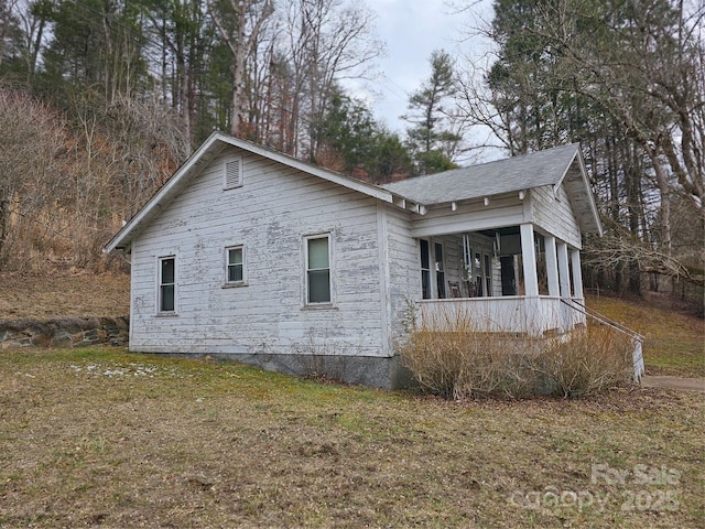 view of side of home with a shingled roof and a lawn