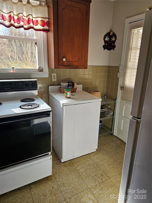 kitchen featuring freestanding refrigerator, electric stove, light countertops, and tile walls