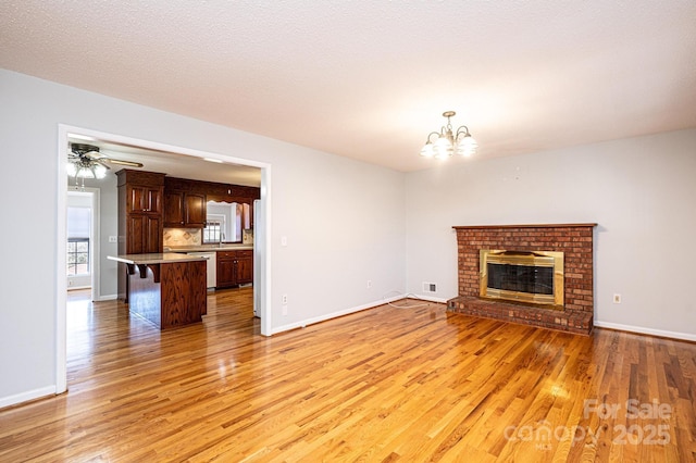 unfurnished living room with ceiling fan with notable chandelier, a fireplace, sink, light hardwood / wood-style floors, and a textured ceiling