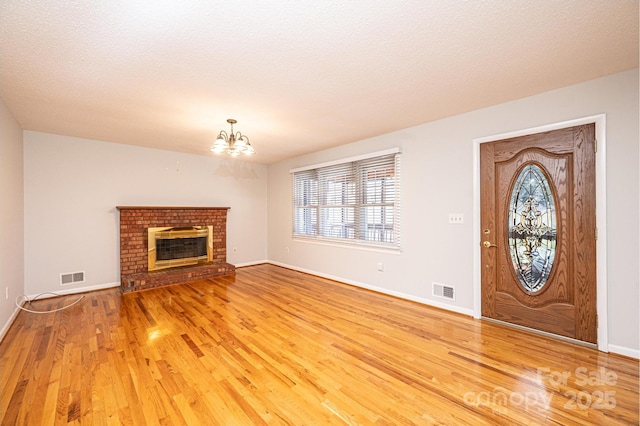 foyer with wood-type flooring, a chandelier, a brick fireplace, and a textured ceiling