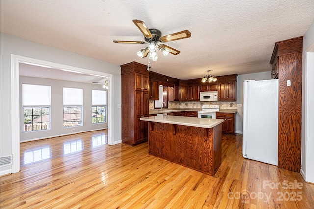 kitchen with white appliances, a center island, tasteful backsplash, light hardwood / wood-style floors, and ceiling fan with notable chandelier