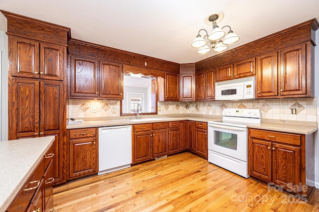 kitchen with sink, backsplash, hanging light fixtures, light hardwood / wood-style floors, and white appliances