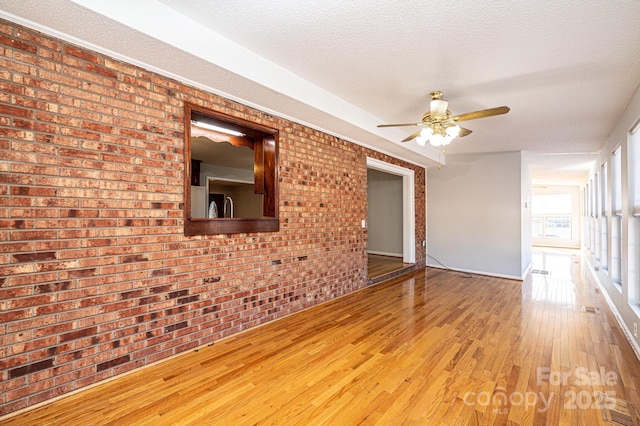 unfurnished room featuring ceiling fan, brick wall, hardwood / wood-style floors, and a textured ceiling