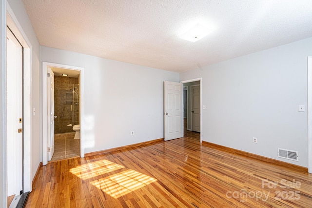 unfurnished bedroom featuring hardwood / wood-style flooring, ensuite bathroom, and a textured ceiling