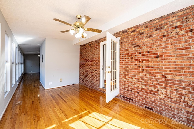 unfurnished room featuring hardwood / wood-style flooring, ceiling fan, brick wall, and a textured ceiling