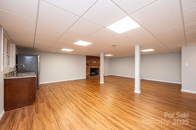 basement with hardwood / wood-style floors, stainless steel refrigerator, a fireplace, sink, and a drop ceiling