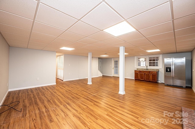 basement featuring stainless steel refrigerator with ice dispenser, wood-type flooring, and a drop ceiling