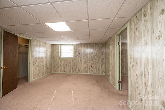 basement featuring a drop ceiling, wooden walls, and carpet