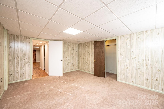 basement featuring carpet, a drop ceiling, and wooden walls