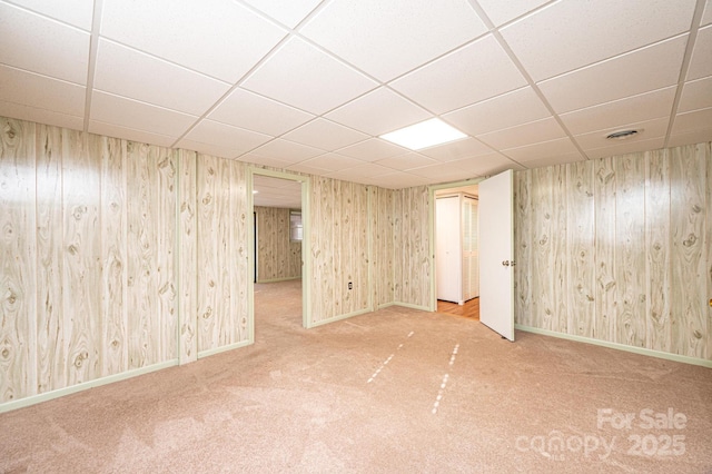 basement featuring a drop ceiling, wooden walls, and carpet flooring