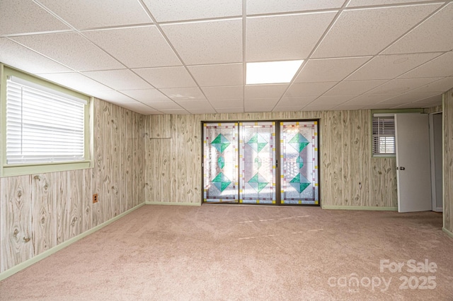 carpeted empty room featuring a paneled ceiling and wood walls