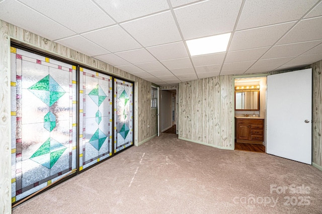 interior space with a paneled ceiling, carpet flooring, sink, and wood walls