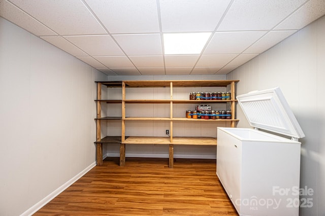 basement featuring wood-type flooring, a paneled ceiling, and refrigerator