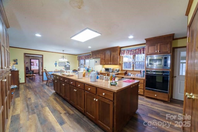 kitchen with pendant lighting, black oven, a center island, stainless steel microwave, and ornamental molding