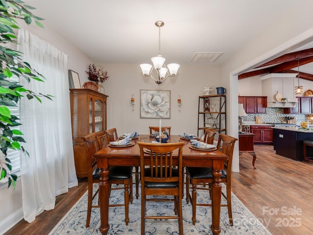 dining room with a chandelier, dark hardwood / wood-style flooring, and beamed ceiling