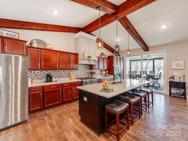 kitchen featuring stainless steel appliances, a kitchen island with sink, pendant lighting, sink, and a kitchen bar