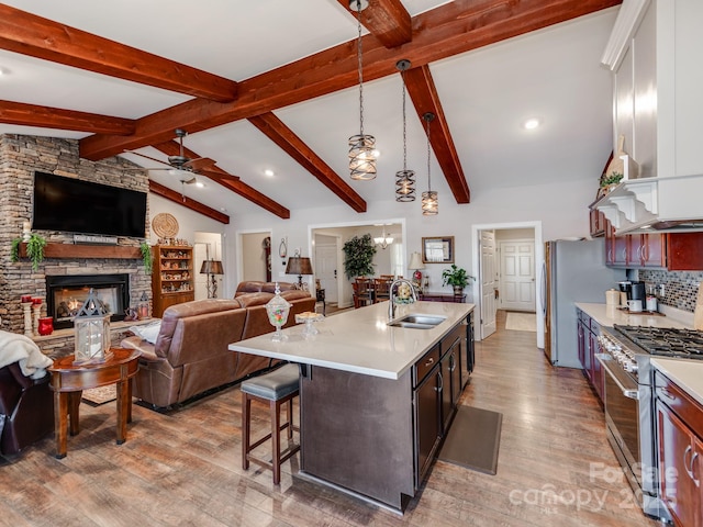 kitchen with a fireplace, a kitchen island with sink, stainless steel appliances, decorative light fixtures, and sink