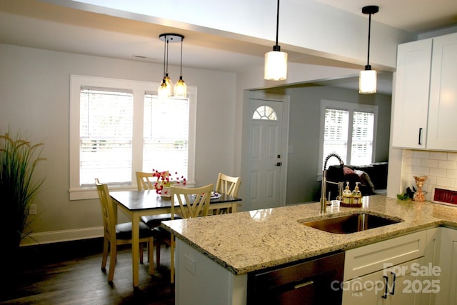 kitchen with sink, light stone counters, white cabinetry, decorative light fixtures, and black dishwasher