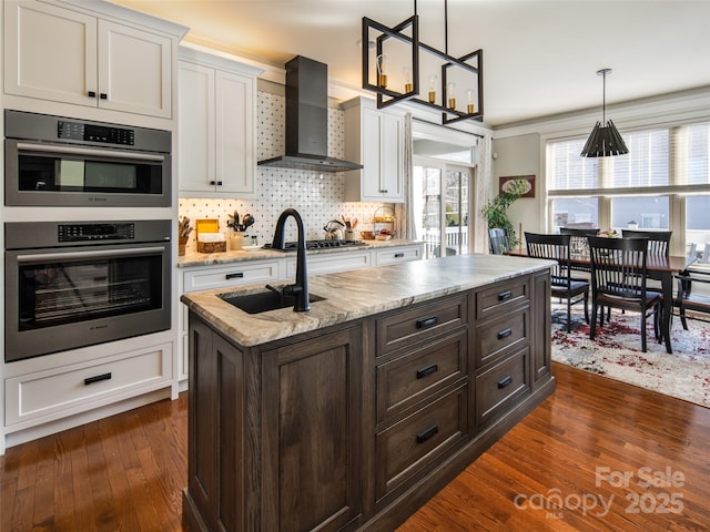 kitchen with white cabinetry, pendant lighting, appliances with stainless steel finishes, and wall chimney range hood