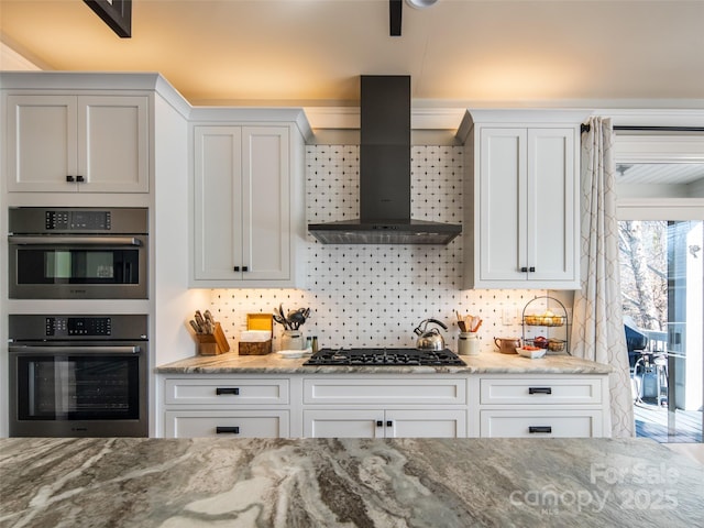 kitchen featuring white cabinetry, tasteful backsplash, wall chimney exhaust hood, and appliances with stainless steel finishes