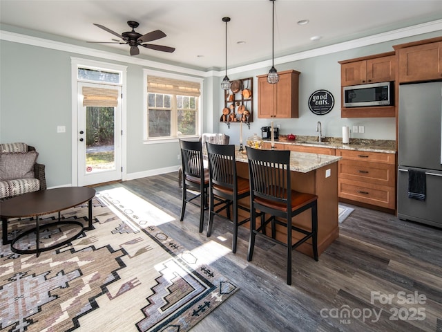 kitchen with dark hardwood / wood-style flooring, hanging light fixtures, ornamental molding, stainless steel appliances, and light stone countertops