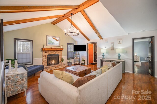 living room with a stone fireplace, dark wood-type flooring, vaulted ceiling with beams, and a notable chandelier