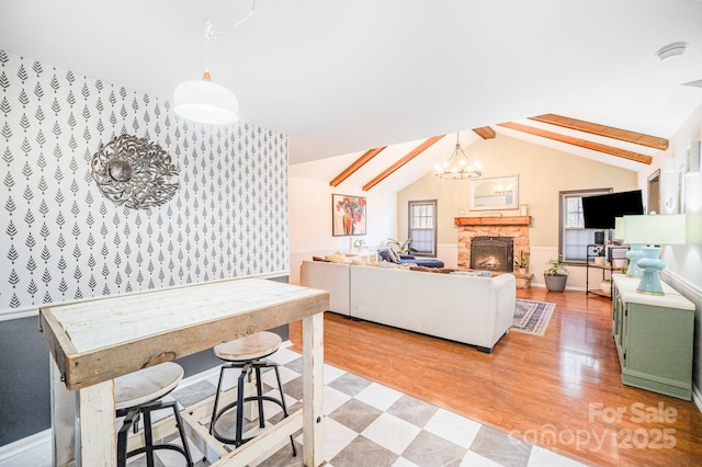 living room featuring lofted ceiling with beams, plenty of natural light, a notable chandelier, and a fireplace