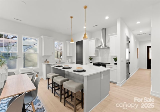 kitchen featuring wall chimney exhaust hood, sink, a kitchen island, pendant lighting, and white cabinets