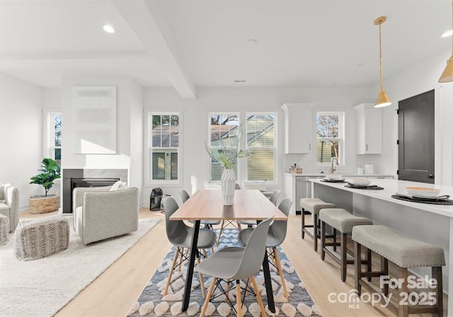 dining area featuring beamed ceiling, a high end fireplace, and light hardwood / wood-style flooring