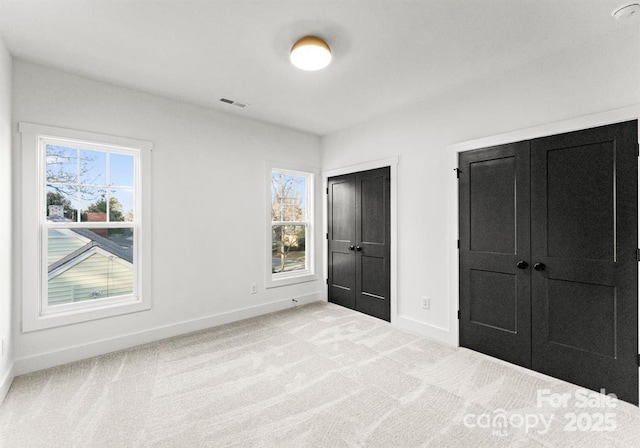 unfurnished bedroom with two closets and light colored carpet