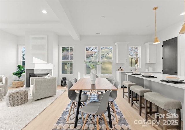 dining area featuring light wood-style floors, beamed ceiling, a fireplace, and recessed lighting