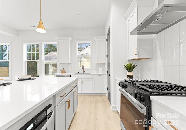 kitchen with black range with gas cooktop, wall chimney exhaust hood, light wood-style flooring, light countertops, and a sink