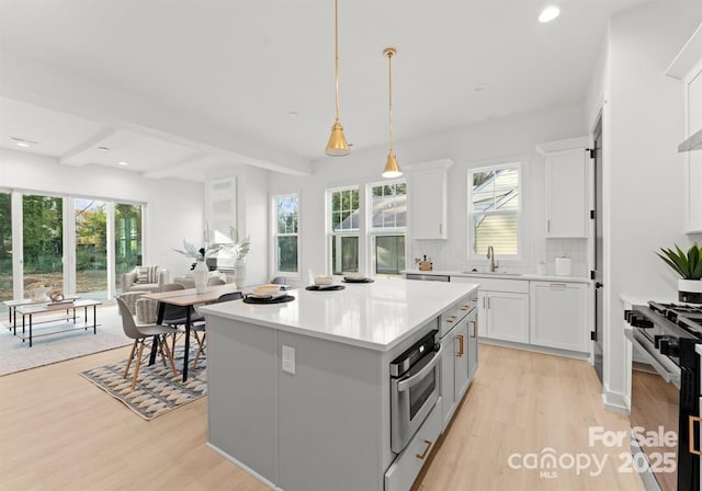 kitchen with range with gas stovetop, a sink, light wood-type flooring, oven, and beamed ceiling