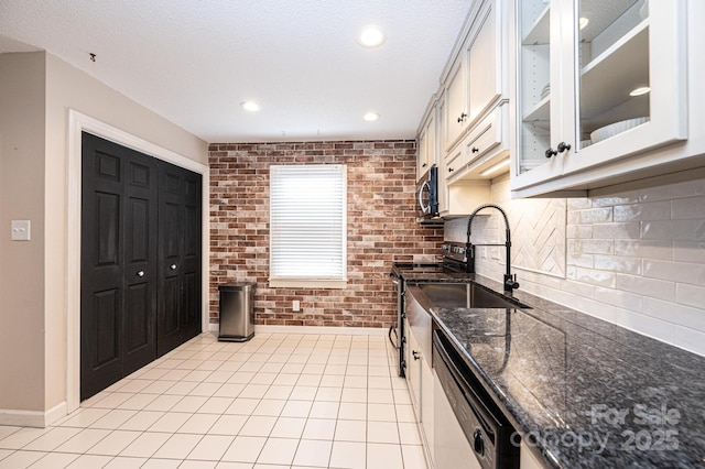 kitchen with stainless steel appliances, white cabinetry, brick wall, and dark stone counters