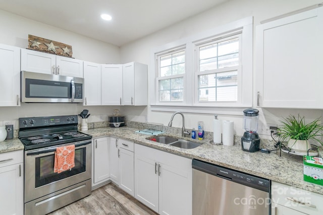 kitchen featuring sink, white cabinetry, appliances with stainless steel finishes, light stone countertops, and light hardwood / wood-style floors