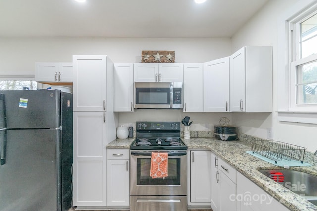 kitchen with white cabinetry, stainless steel appliances, sink, and light stone counters