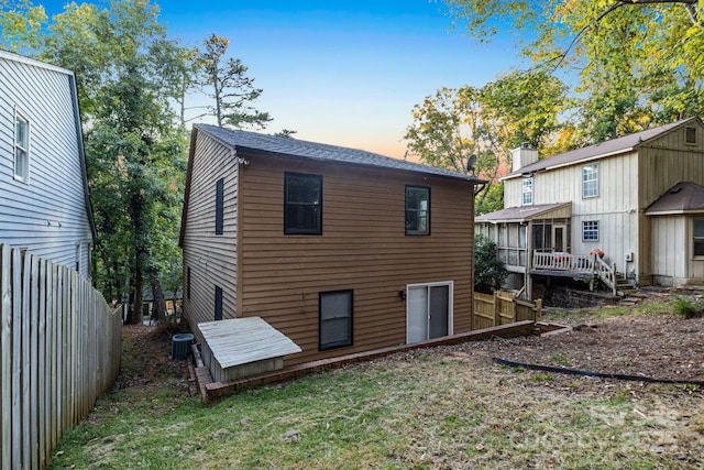 back house at dusk featuring a wooden deck, a yard, and central air condition unit